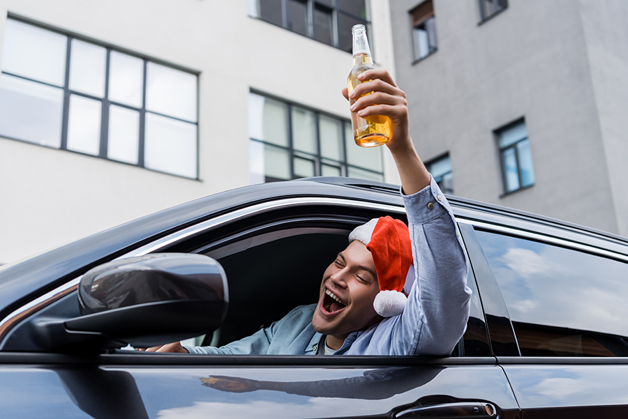 Mann mit Weihnachtsmütze und Bierflasche in der Hand schreit aus dem offenen Autofenster