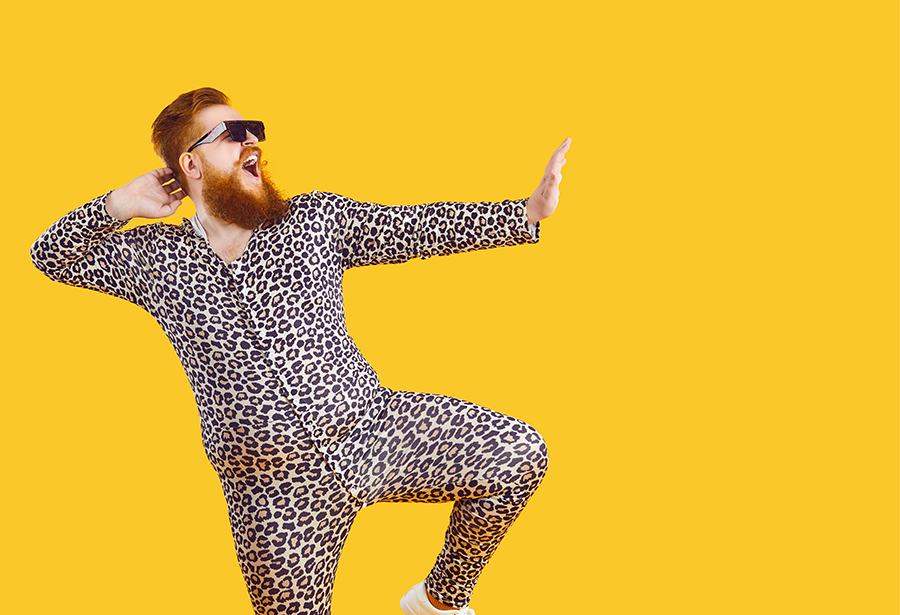 Mann mit Bart und Sonnenbrille im Leopardenpyjama tanzt vor gelbem Hintergrund