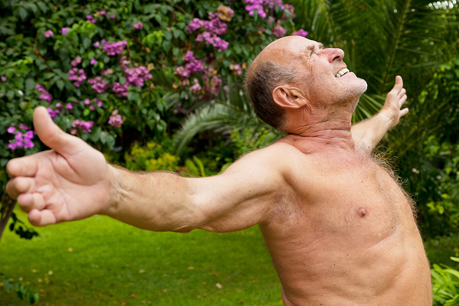 Nackter Mann breitet im Garten die Arme aus